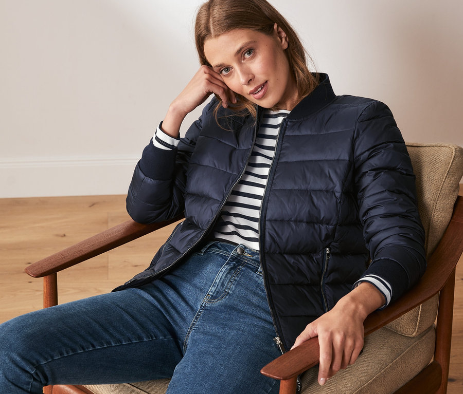 Frau sitzt im Sessel und trägt eine Steppjacke.