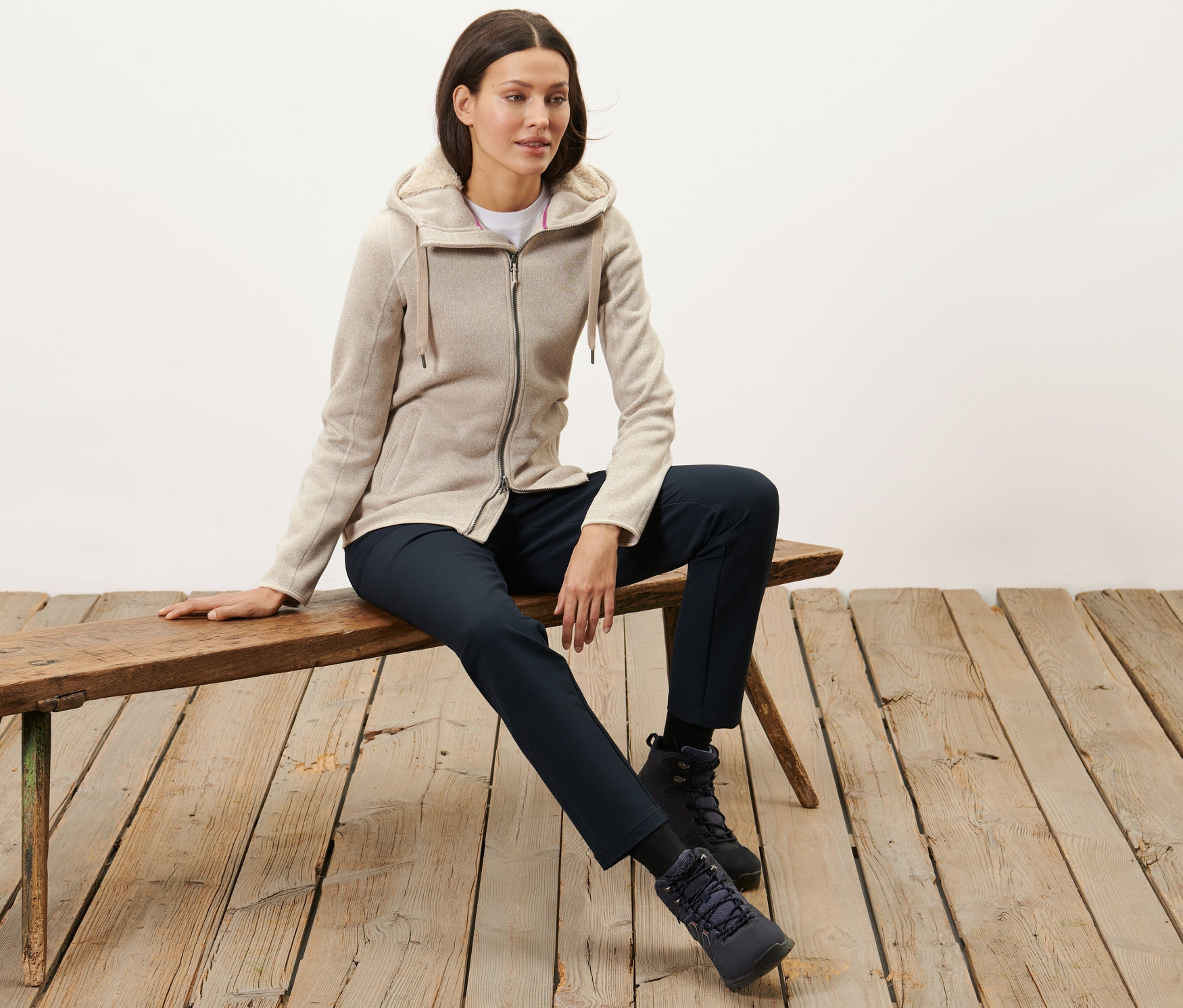 Frau sitzt auf Bank und trägt eine sandfarbene Kapuzen-Strickfleecejacke.