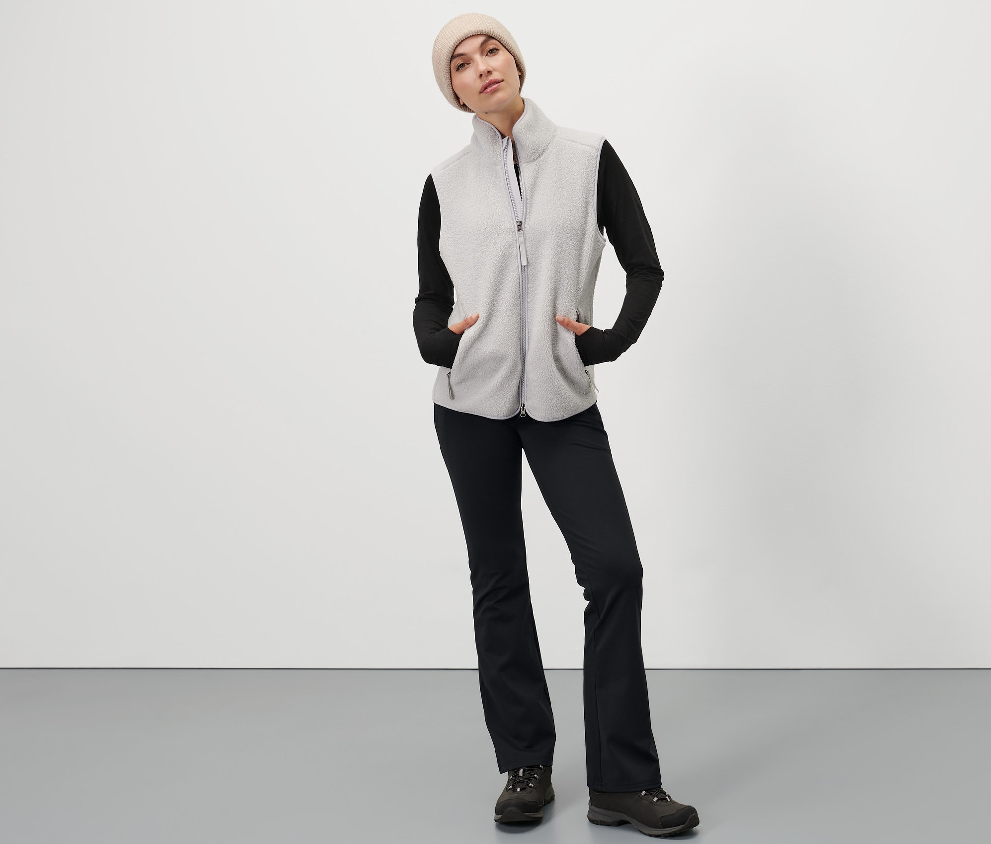 Frau posiert in Thermo-Jazzpants, Weste und Mütze.