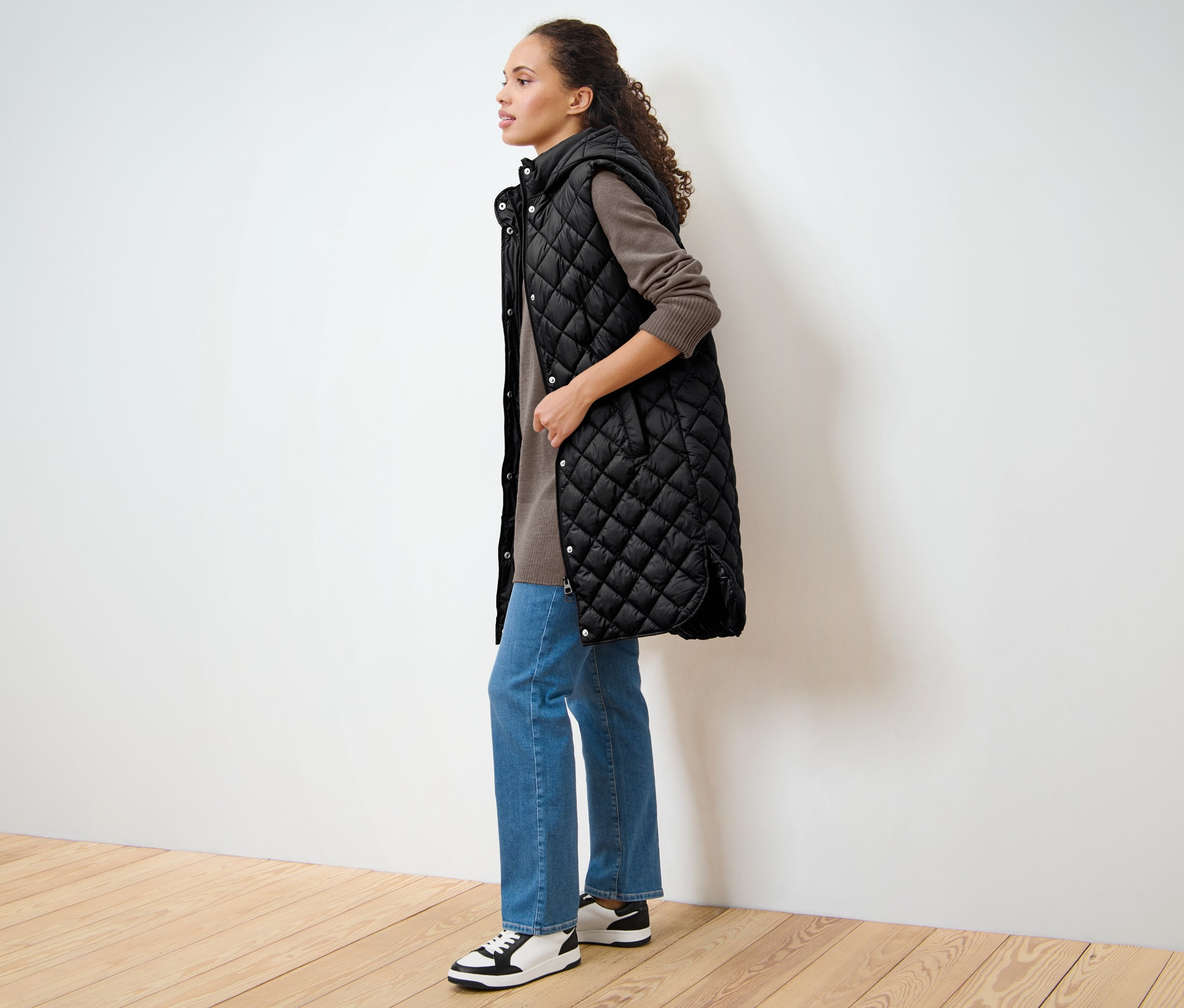 Frau steht seitlich und trägt eine lange Steppweste mit Kapuze.