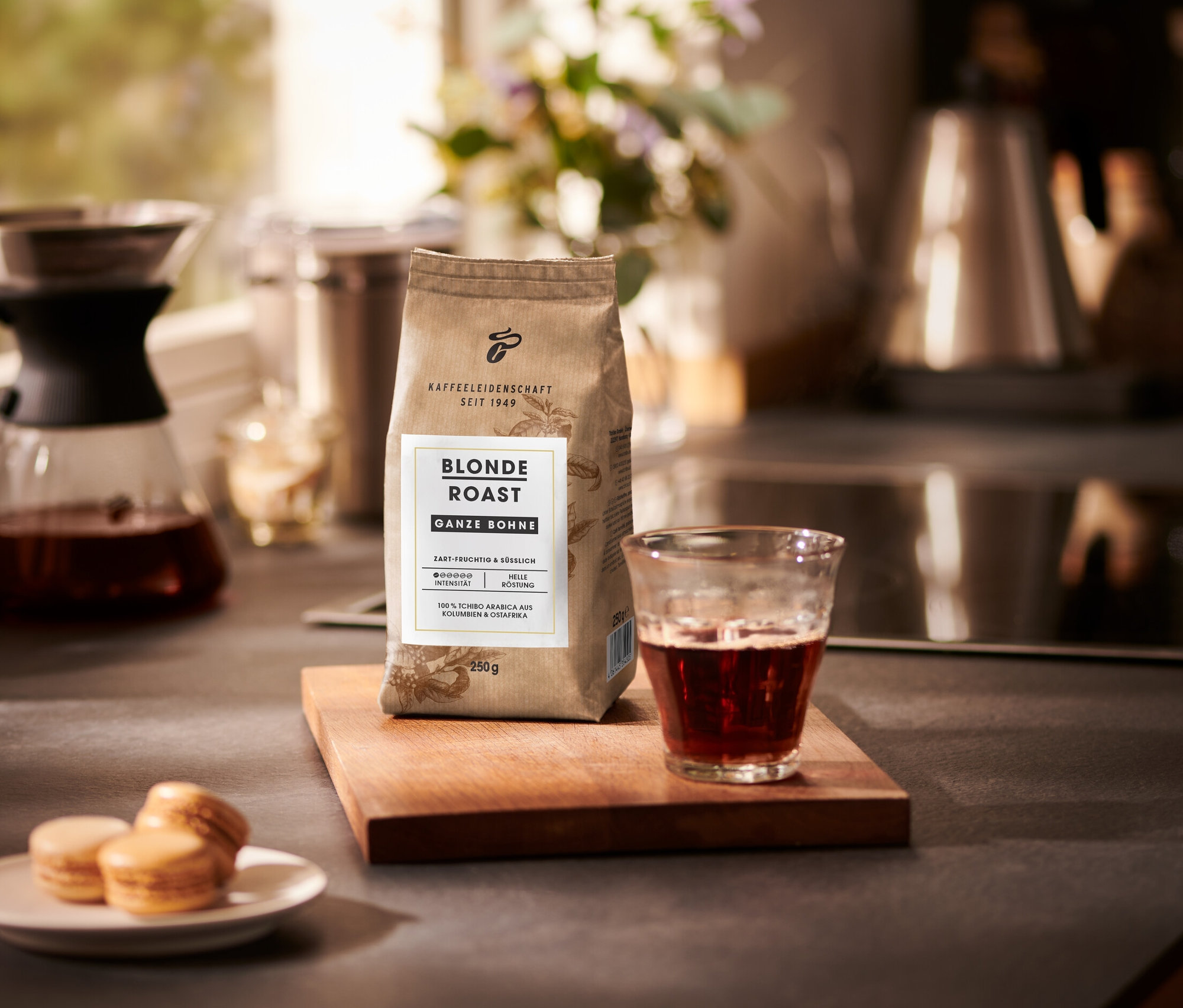 Eine Packung Blonde Roast - Ganze Bohne Kaffee neben einem Glas Kaffee und einem Teller Macarons.