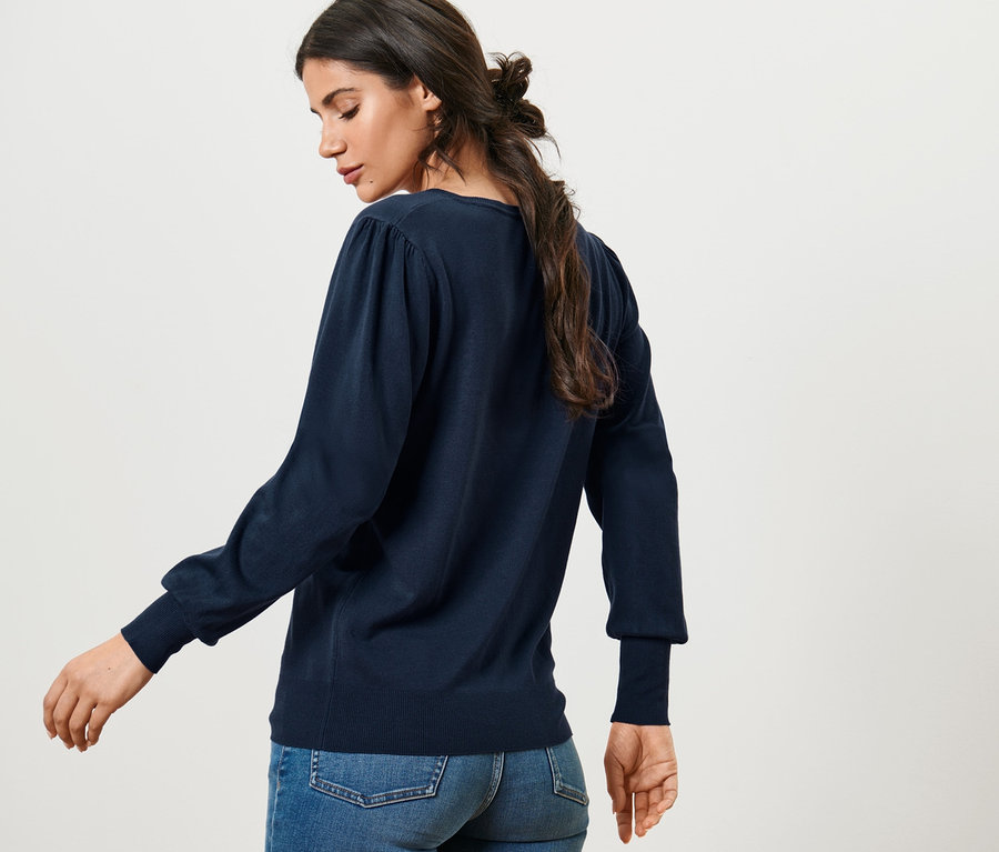 Frau posiert in Feinstrickpullover und Jeans.