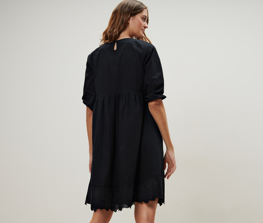 Frau steht mit dem Rücken zur Kamera und trägt ein schwarzes Webkleid mit Stickerei.