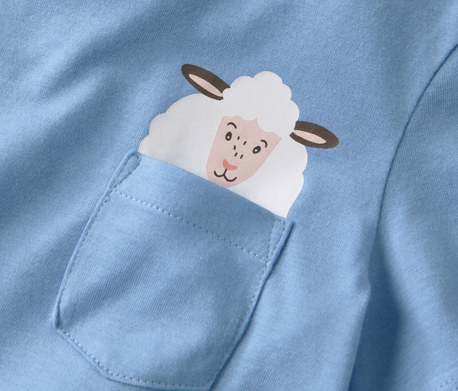 Detailansicht eines blauen T-Shirts mit einer aufgesetzten Tasche, aus der ein Schafkopf herausschaut.