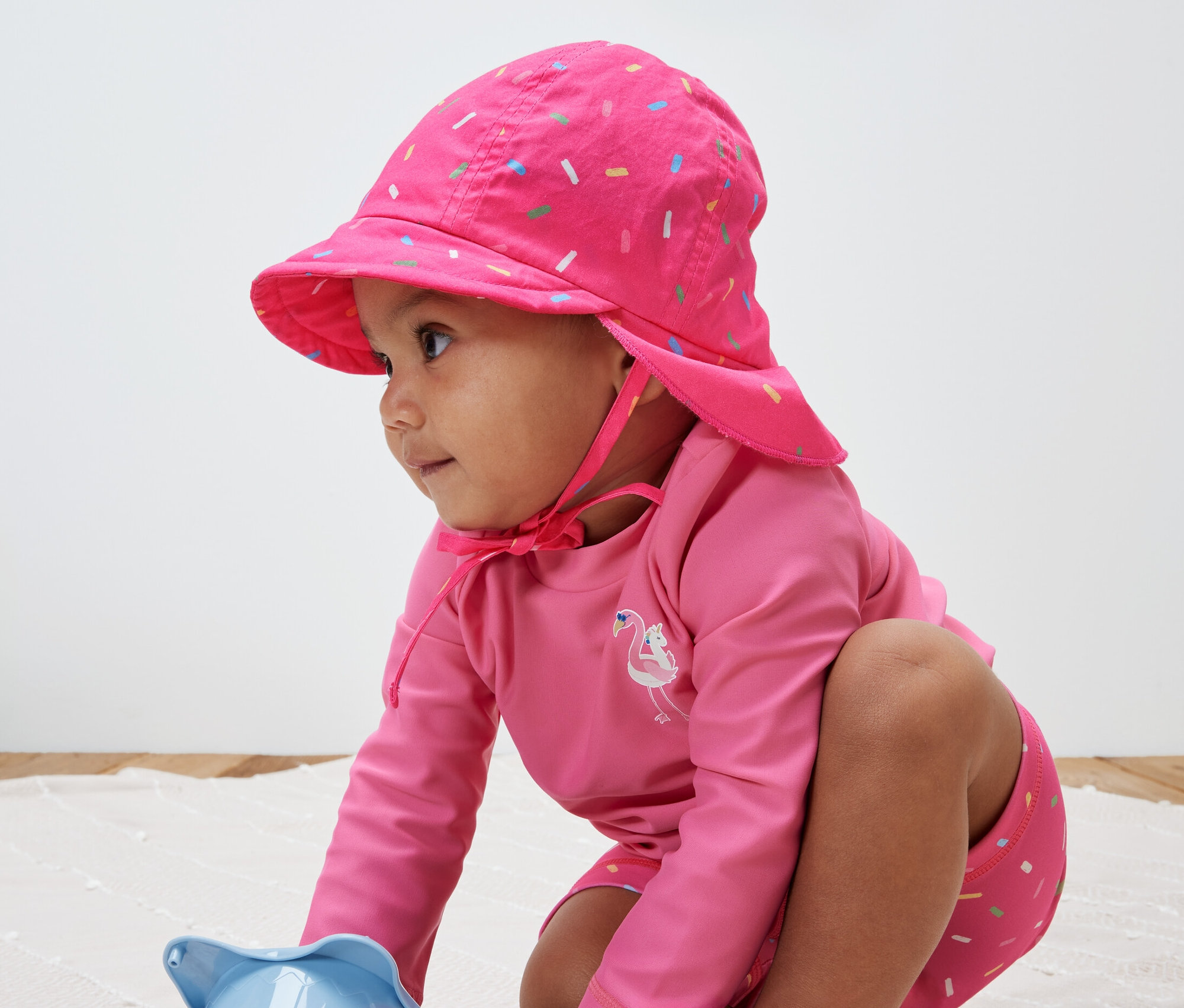 Kind spielt mit Spielzeug und trägt eine pinke Kinder-Sonnenmütze mit UV-Schutzfaktor 80.
