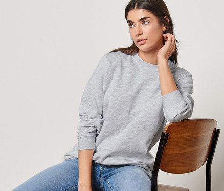 Frau sitzt auf einem Stuhl und trägt ein graues Sweatshirt.