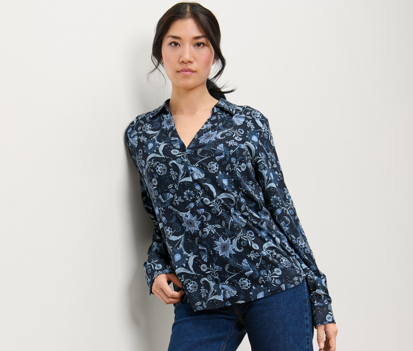 Frau posiert in einem bedruckten Blusenshirt mit Knopfleiste und Jeans.