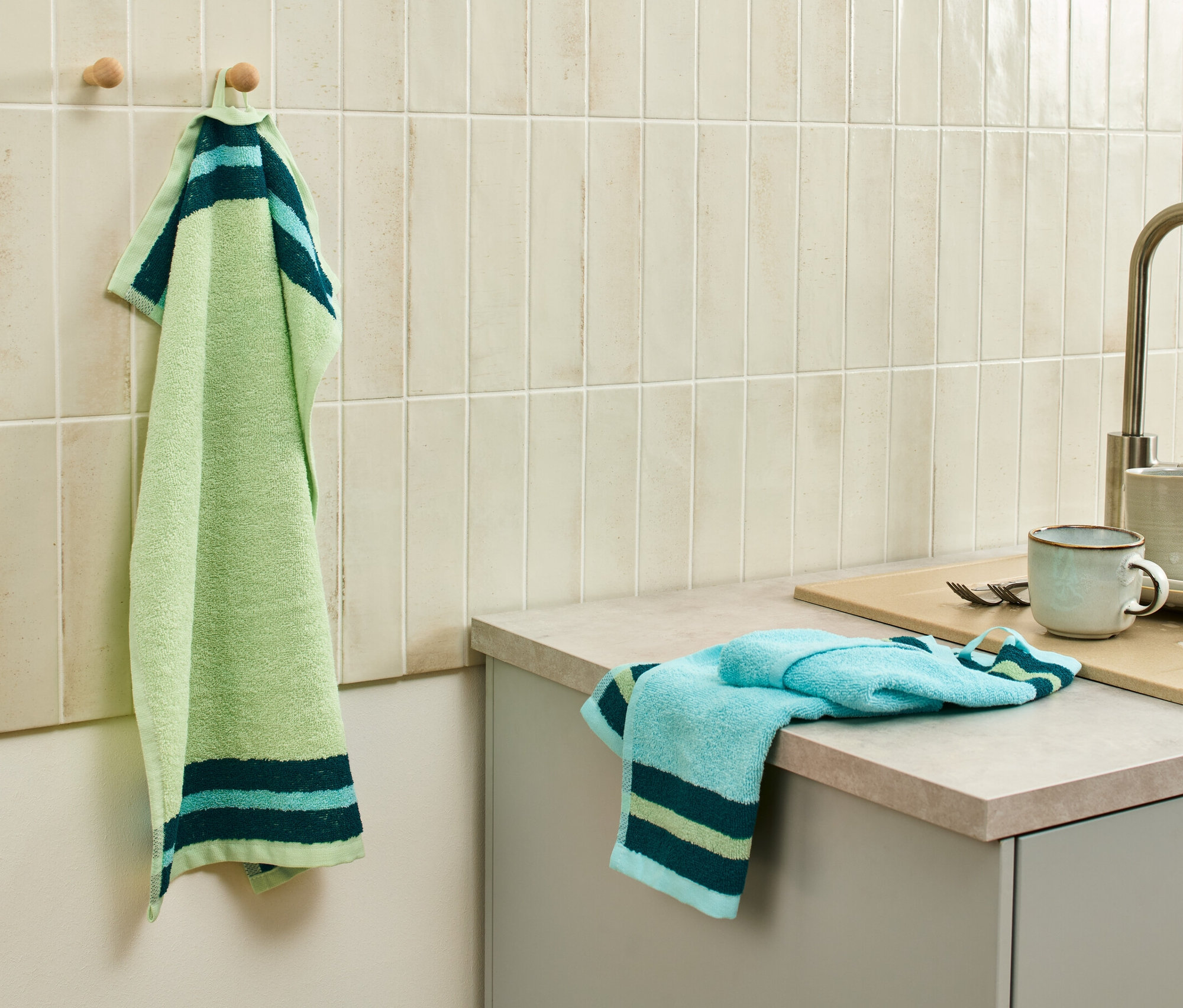 Ein grün-blaues Küchentuch hängt an einem Haken neben der Spüle, weitere 2 Küchenhandtücher liegen auf der Arbeitsfläche.