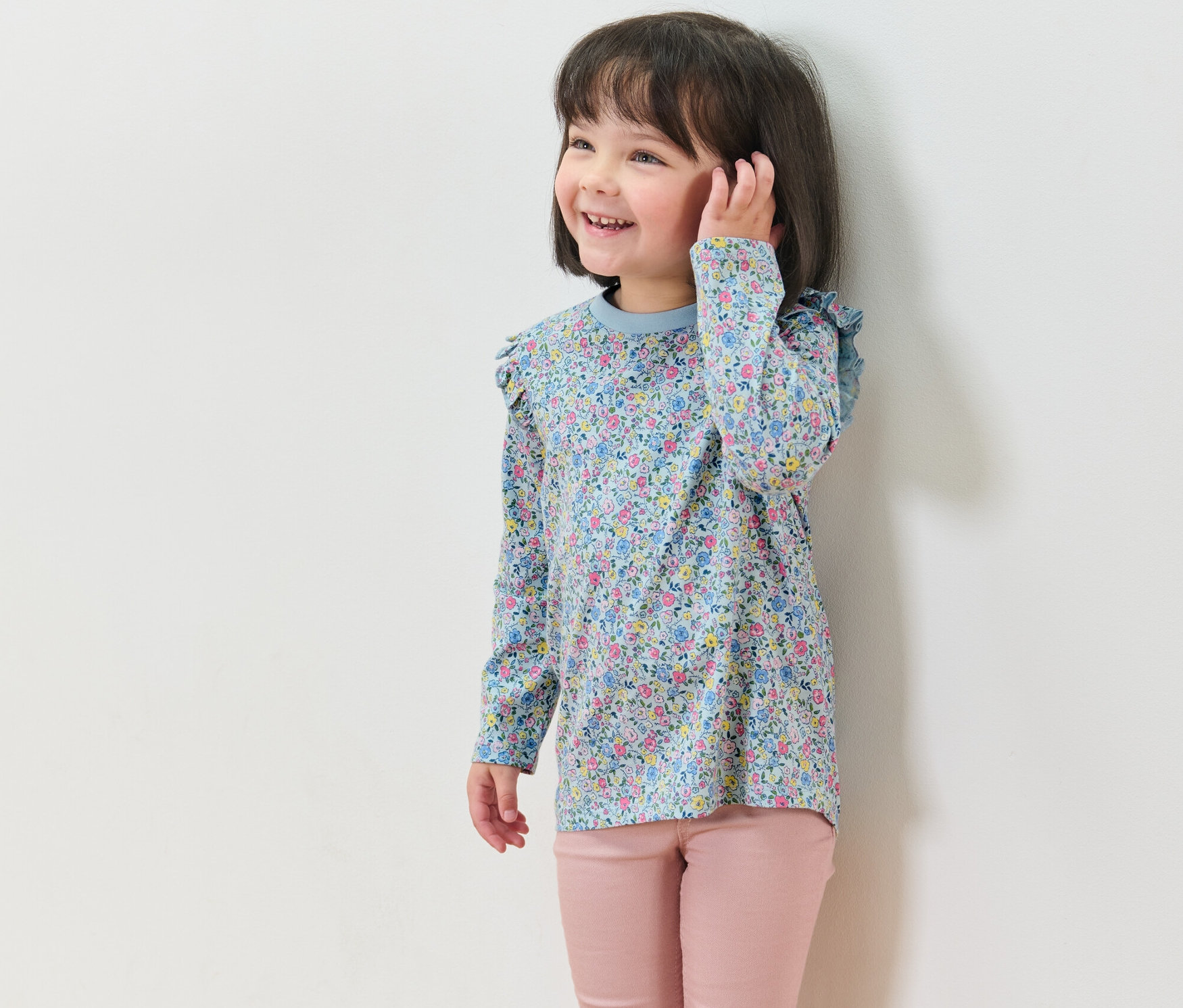 Lächelndes Mädchen trägt ein geblümtes Langarmshirt aus einem 2er-Set und eine rosafarbene Hose.