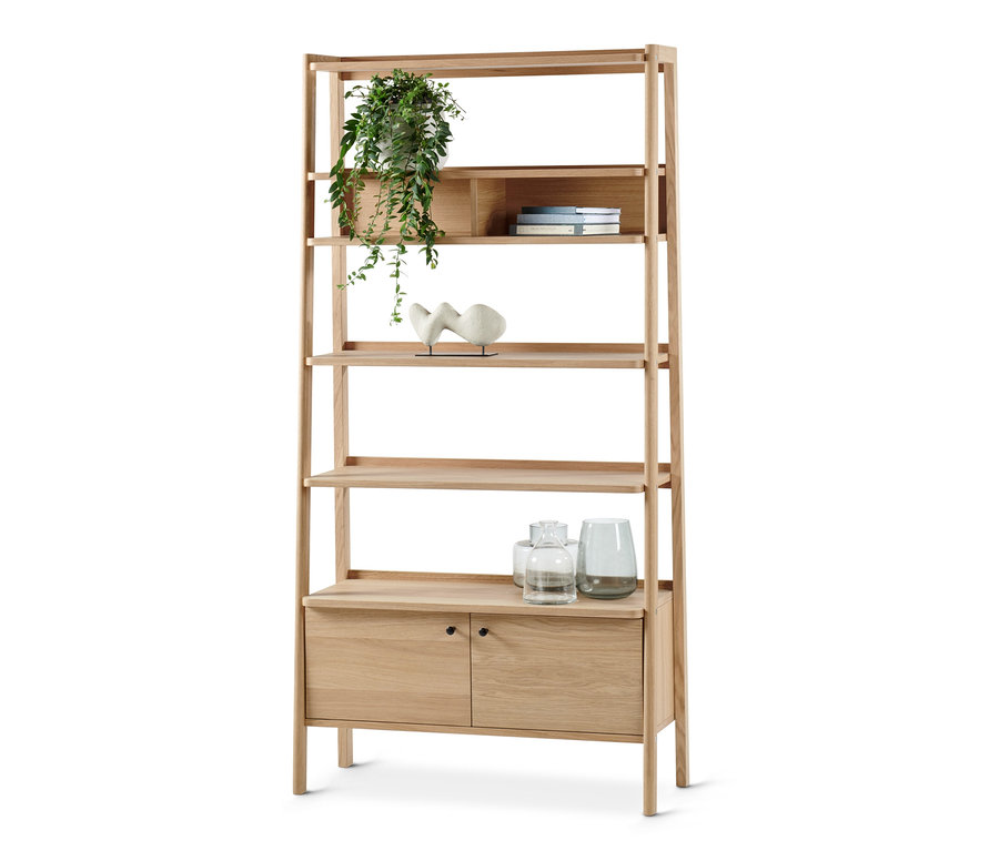 Ein helles Holzregal mit fünf offenen Fächern und einem Schrankteil mit zwei Türen. Auf den Fächern stehen Pflanzen, Bücher, Vasen und eine Skulptur.