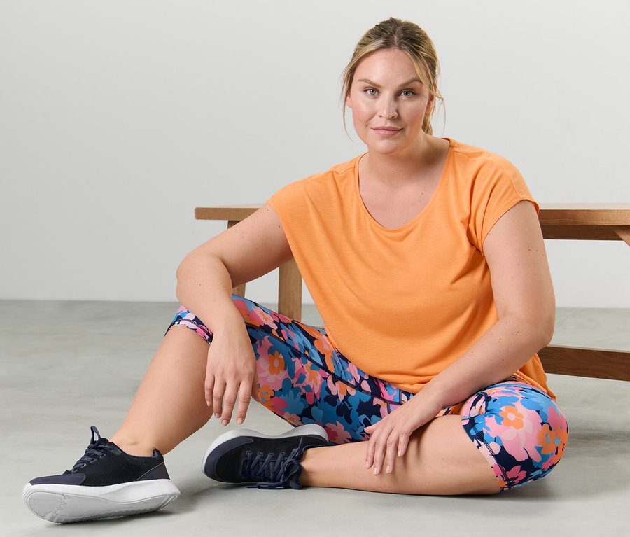 Frau sitzt auf dem Boden und trägt ein pfirsichfarbenes Sportshirt.