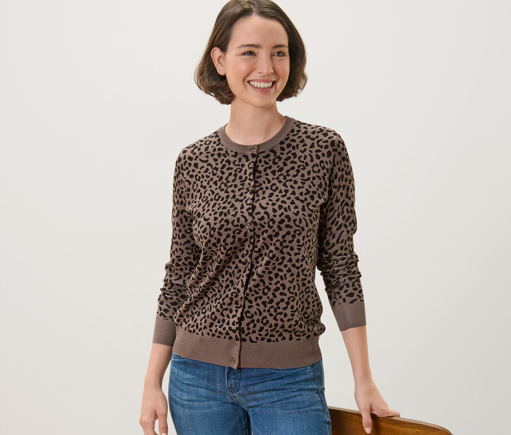 Frau trägt einen bedruckten Feinstrick-Cardigan und lehnt an einem Stuhl.