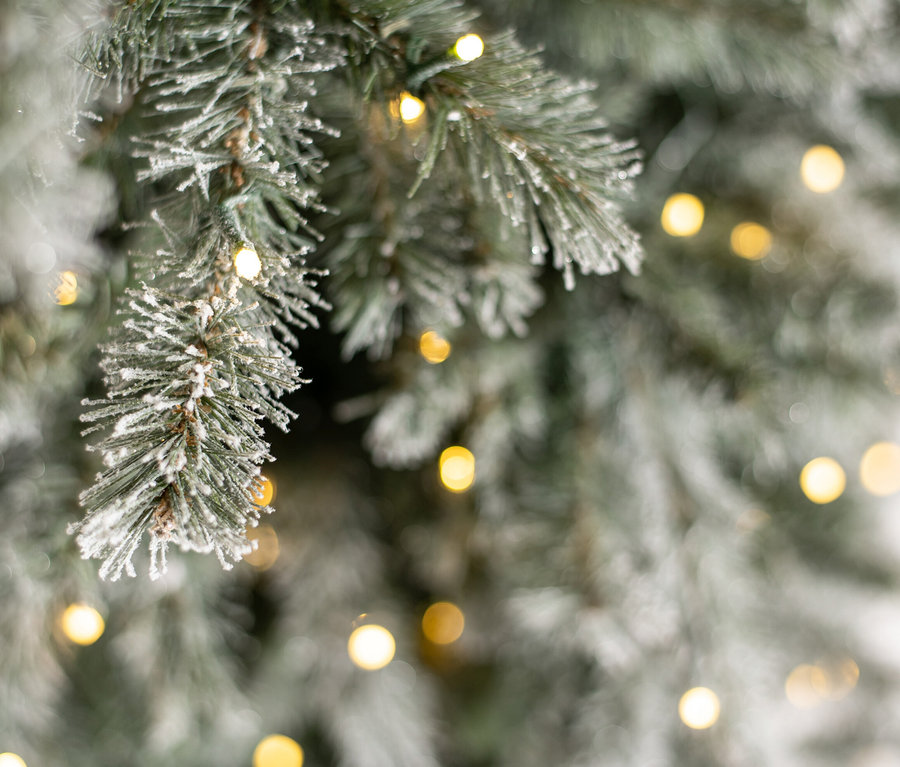 Nahaufnahme eines beschneiten künstlichen Weihnachtsbaums "Fichte" mit LED-Lichterkette.