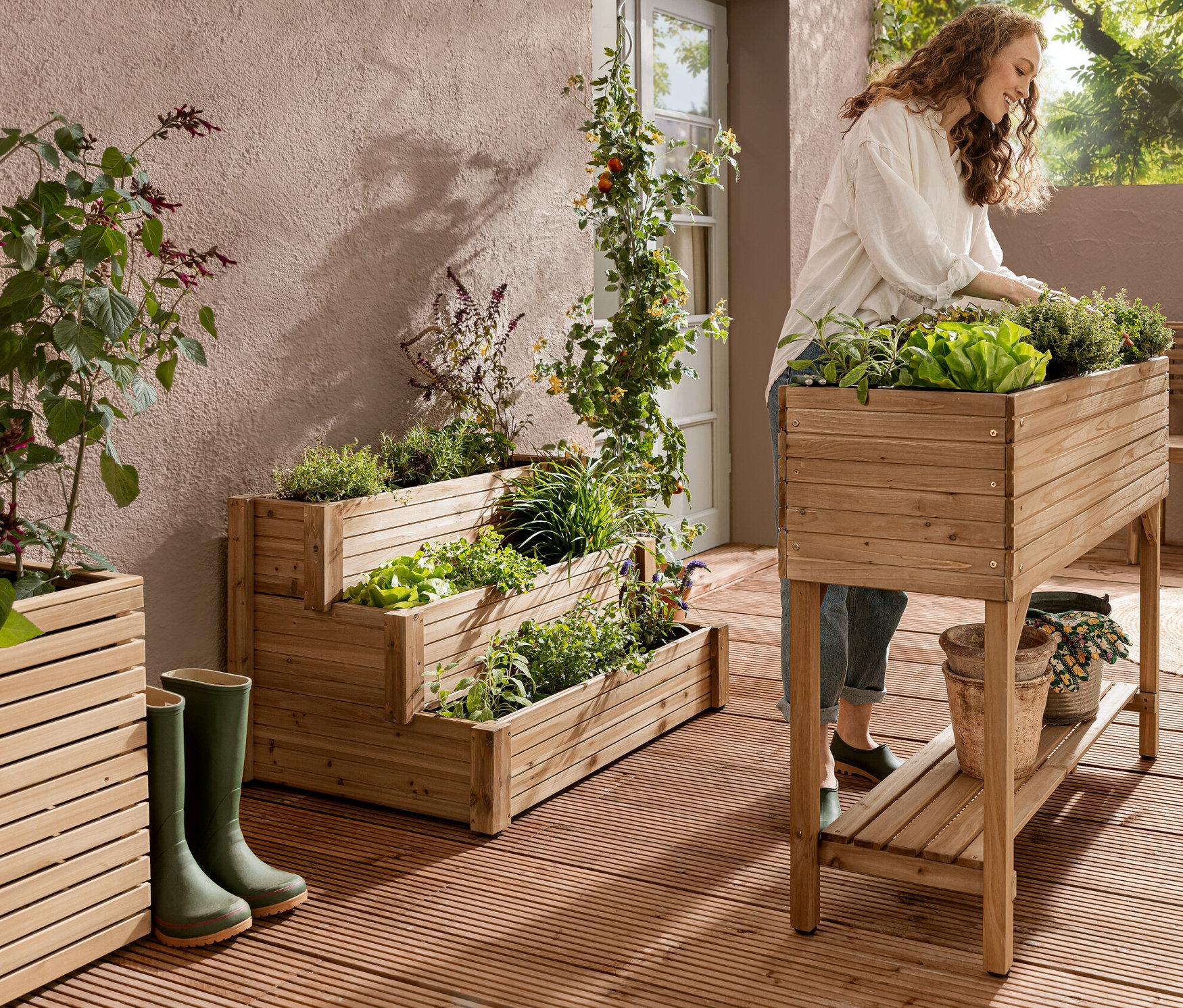 Eine Frau arbeitet an einem Hochbeet mit Regal »Tinus«. Im Hintergrund ist ein Treppenhochbeet mit 3 Ebenen »Tinus« zu sehen.