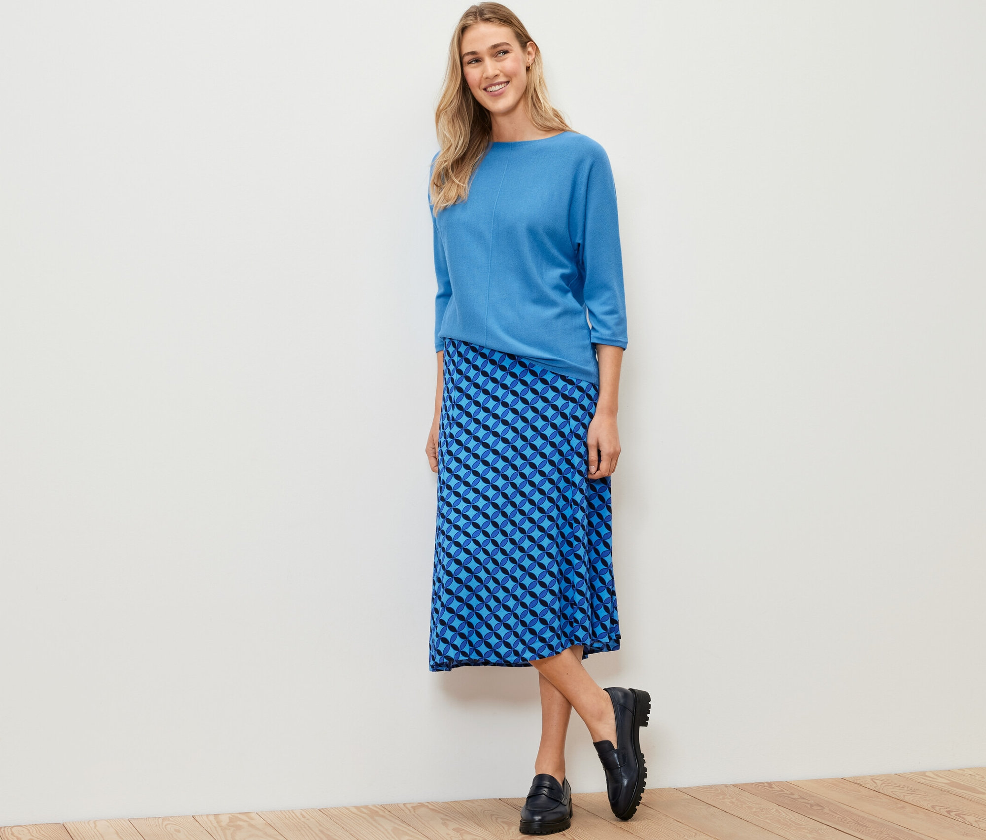 Frau posiert in kobaltblauem Merino-Feinstrickpullover und blauem Rock.