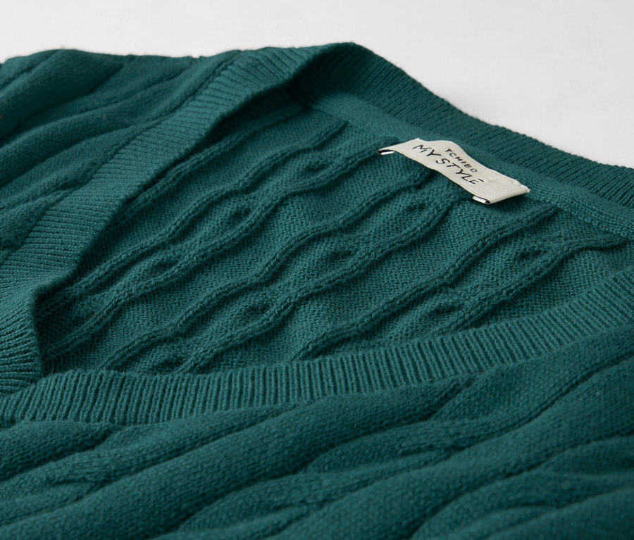 Nahaufnahme eines smaragdgrünen Zopfmuster-Pullovers mit V-Ausschnitt und einem Etikett.