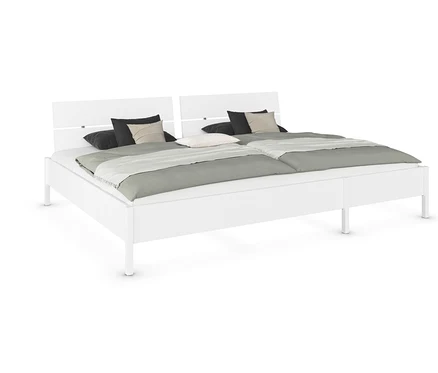 Weißes Doppelbett mit zwei Liegeflächen, Kissen und grauem Überwurf.