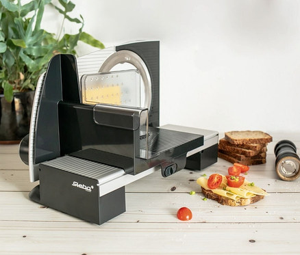 Ein Steba Allesschneider »AS 200« steht neben Brot und Gewürzen auf einem Holztisch.