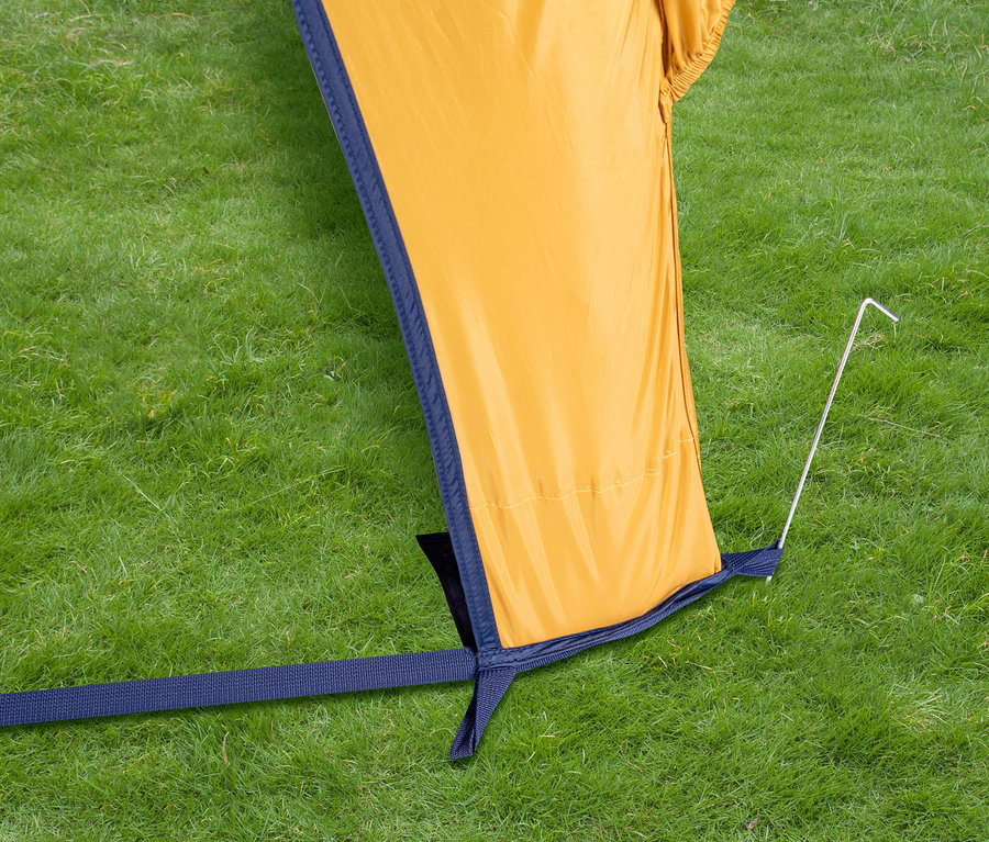 Detailaufnahme eines gelben Tambu Bus-Sonnensegel GATI, das mit einem Hering im Gras befestigt ist.