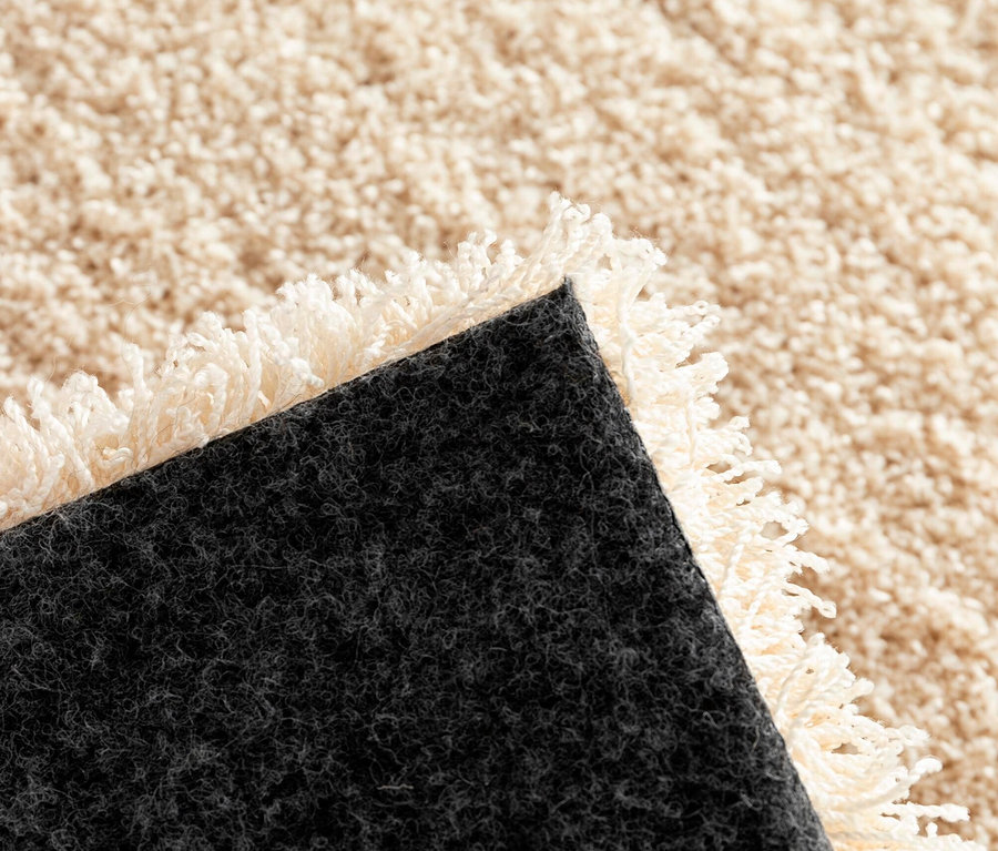 Detailansicht einer Ecke des beigefarbenen Shaggy-Teppichs "Mellow" mit Fransen.
