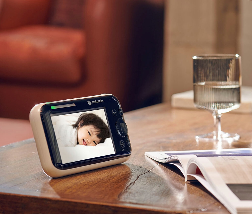 WLAN-Video-Babyphone »PIP1610« auf einem Tisch neben einem Glas Wasser und einer Zeitschrift.