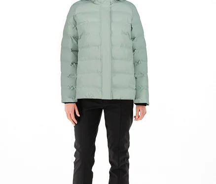 Frau trägt eine hellgrüne CMP Damen-Steppjacke mit Kapuze, schwarze Hose, schwarze Kappe und helle Stiefel.