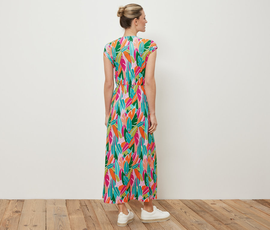 Eine Frau steht mit dem Rücken zur Kamera und trägt ein Jerseykleid mit Knoten und weiße Turnschuhe.