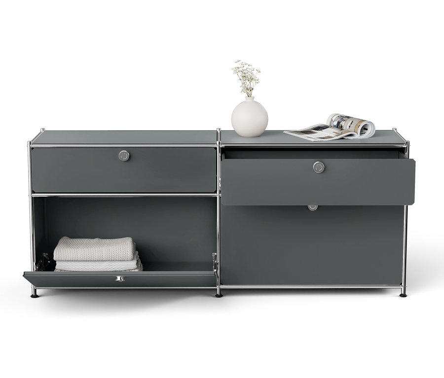 Grauer Schrank mit silbernem Rahmen, offene Schublade, weiße Vase mit Blumen und Zeitschrift oben drauf.