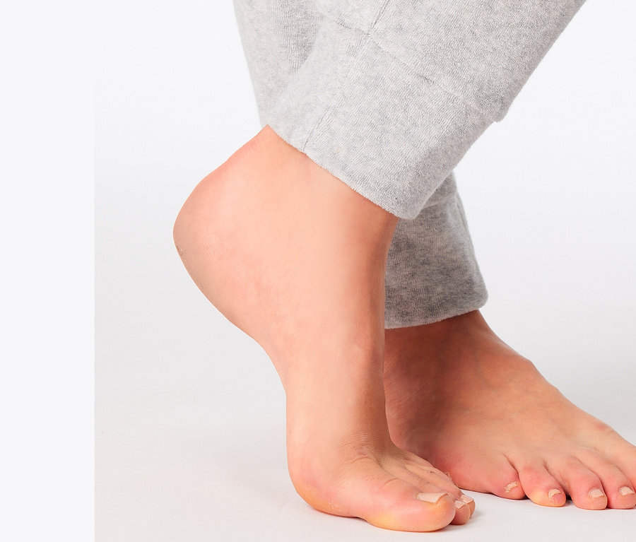 Füße einer Person, die auf einem weißen Hintergrund steht und eine graue Trainingshose trägt.