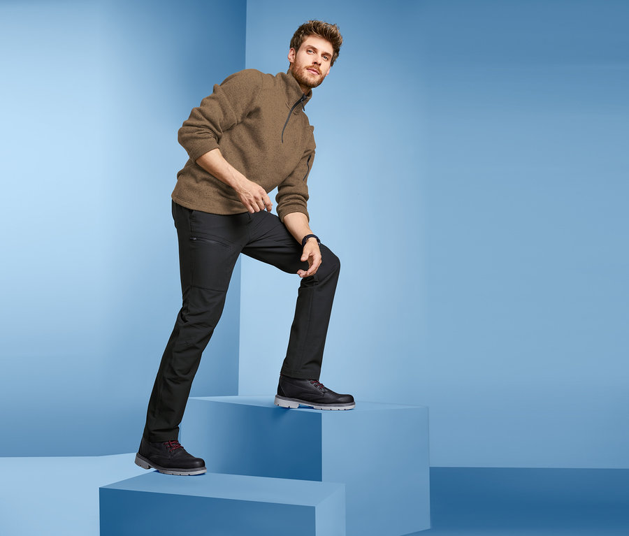 Mann steigt blaue Stufen hoch, trägt einen braunen Pullover und eine schwarze Outdoor-Thermohose.