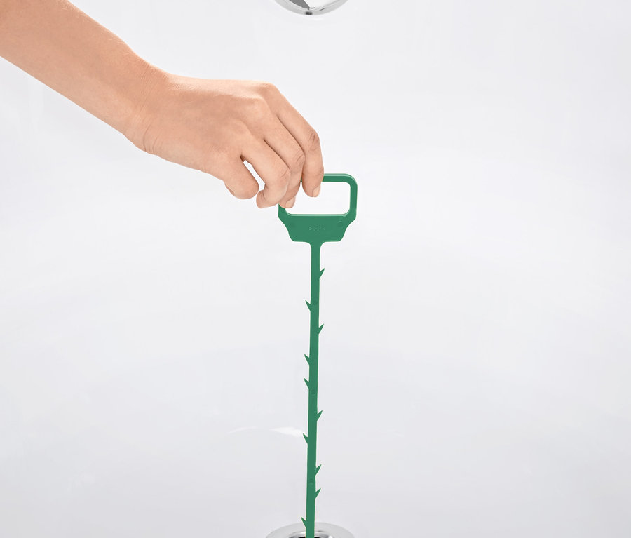 Eine Hand führt einen grünen Abflussreiniger in den Abfluss einer Badewanne ein.