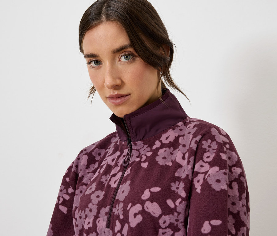 Porträt einer Frau in einer burgunderfarbenen Jacke mit Blumenmuster.