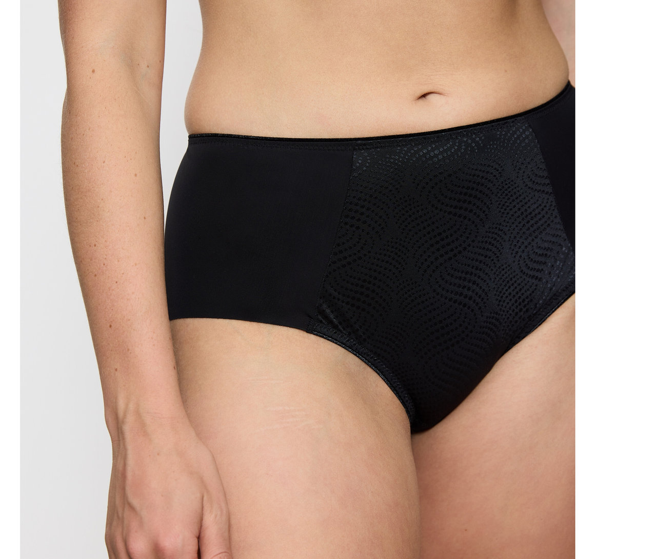 Eine Person trägt schwarze Triumph Essential Minimizer Hipster X Slips mit glatten Seiten und einem strukturierten, gemusterten Vorderteil.