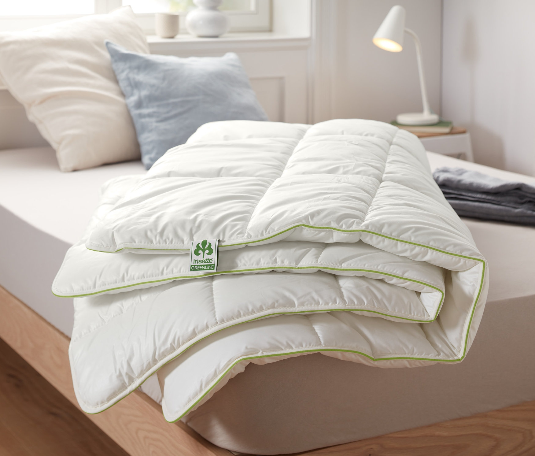 Ein zusammengelegtes irisette® greenline Thermobett mit weißer Oberfläche und grüner Bordüre liegt auf einem Bett.