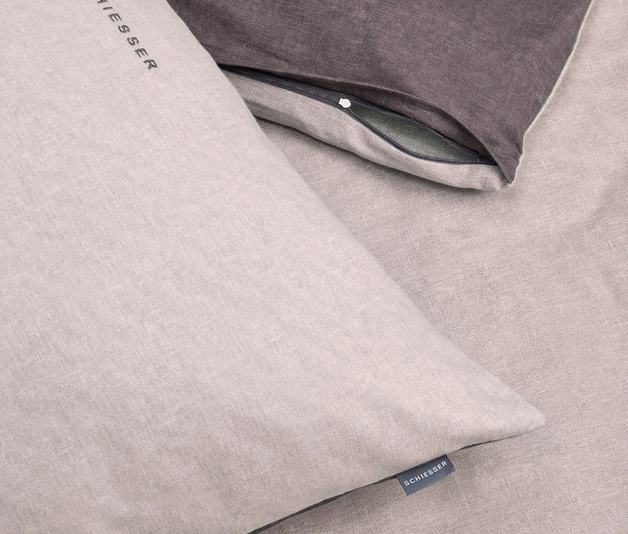 Detailaufnahme einer beigen Bettwäsche und eines grauen Kissens.