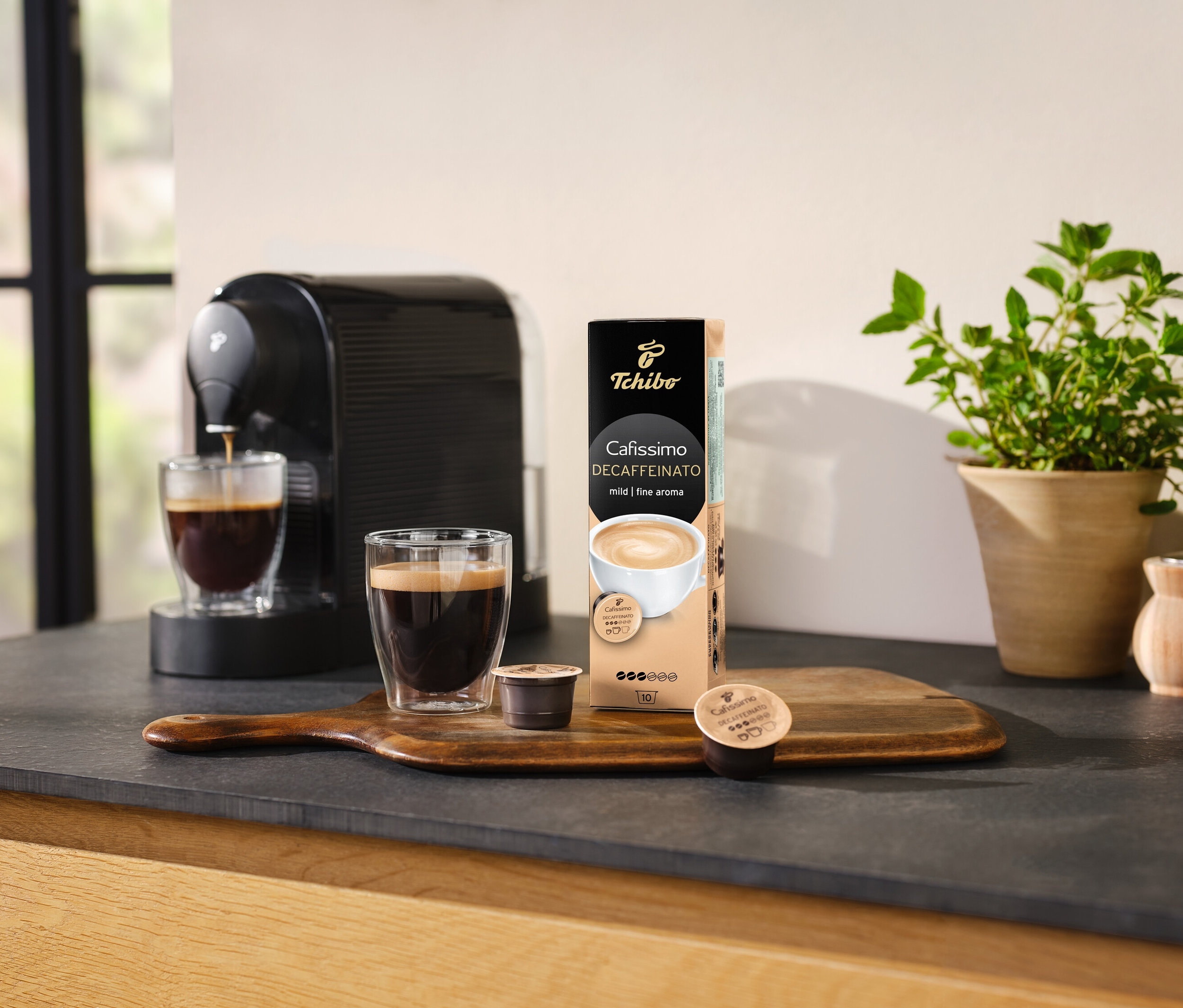 Kaffeemaschine gießt Kaffee in ein Glas neben einer Packung Cafissimo Decaffeinato - entkoffeiniert - 10 Kapseln.