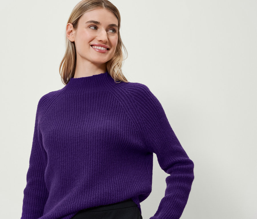 Eine Frau lächelt und trägt einen lila Pullover.