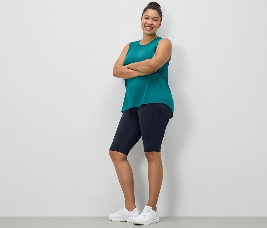 Frau posiert in dunkelblauen Sportradlern und einem türkisfarbenen Sport-Top aus einem 2er-Set.