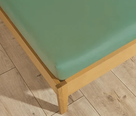 Detailaufnahme eines Bettgestells mit einem grünen Spannbettlaken der SCHÖNER WOHNEN-Kollektion in Normalgröße.