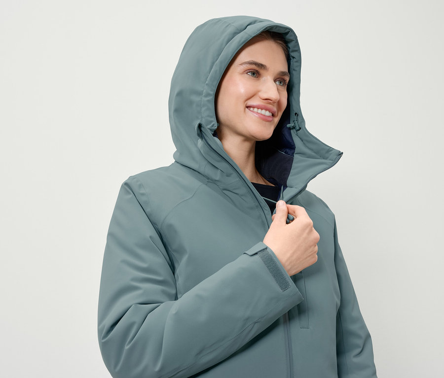 Frau schliesst eine blaugrüne Jacke mit Kapuze.