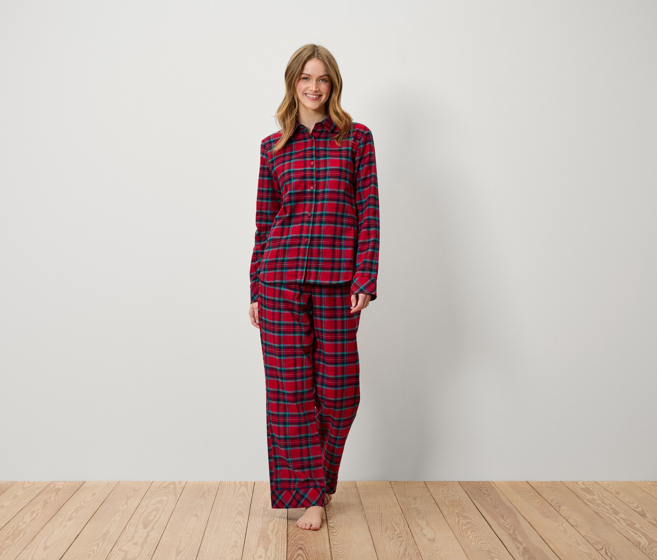Frau steht und lächelt, gekleidet in einem rot karierten Pyjama.