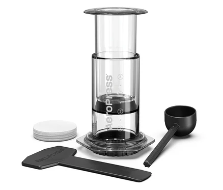 Aeropress Kaffeebereiter mit Zubehör auf weißem Hintergrund.