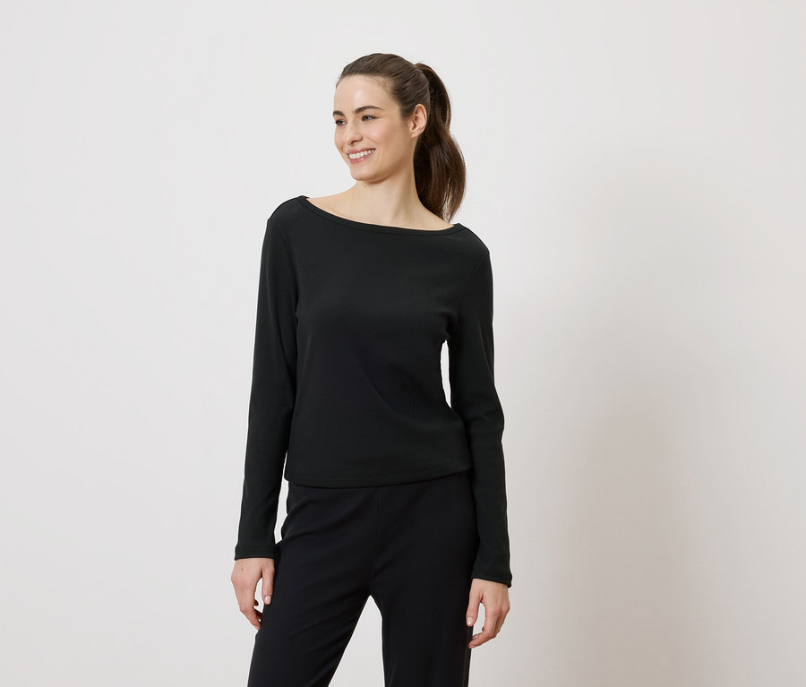Frau mit Pferdeschwanz, die ein schwarzes Langarmshirt und eine schwarze Hose trägt und lächelt.