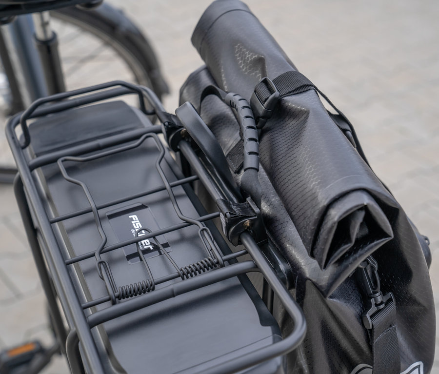 Eine schwarze FISCHER Gepäckträgertasche PLUS+ Terra ist an einem Fahrradgepäckträger befestigt.