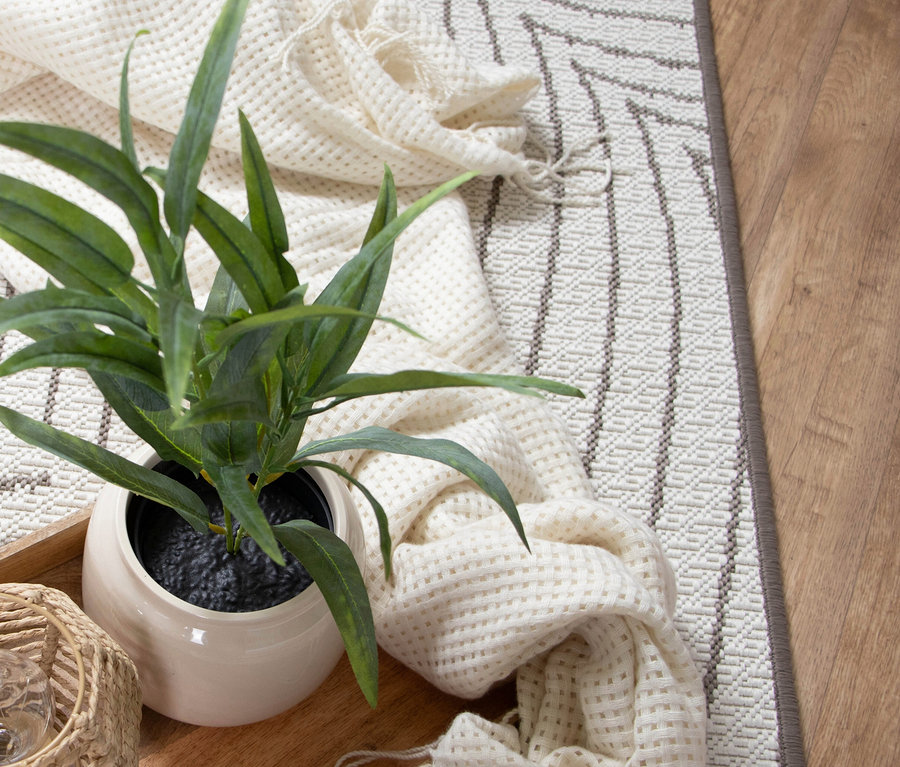 Nahaufnahme einer Zimmerpflanze in einem Topf auf einem Holztablett, zusammen mit einer cremefarbenen Decke auf einem gemusterten Teppich.