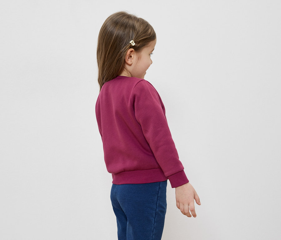 Mädchen mit Haarspange, bordeauxrotem Pullover und blauen Jeans, von hinten gesehen.