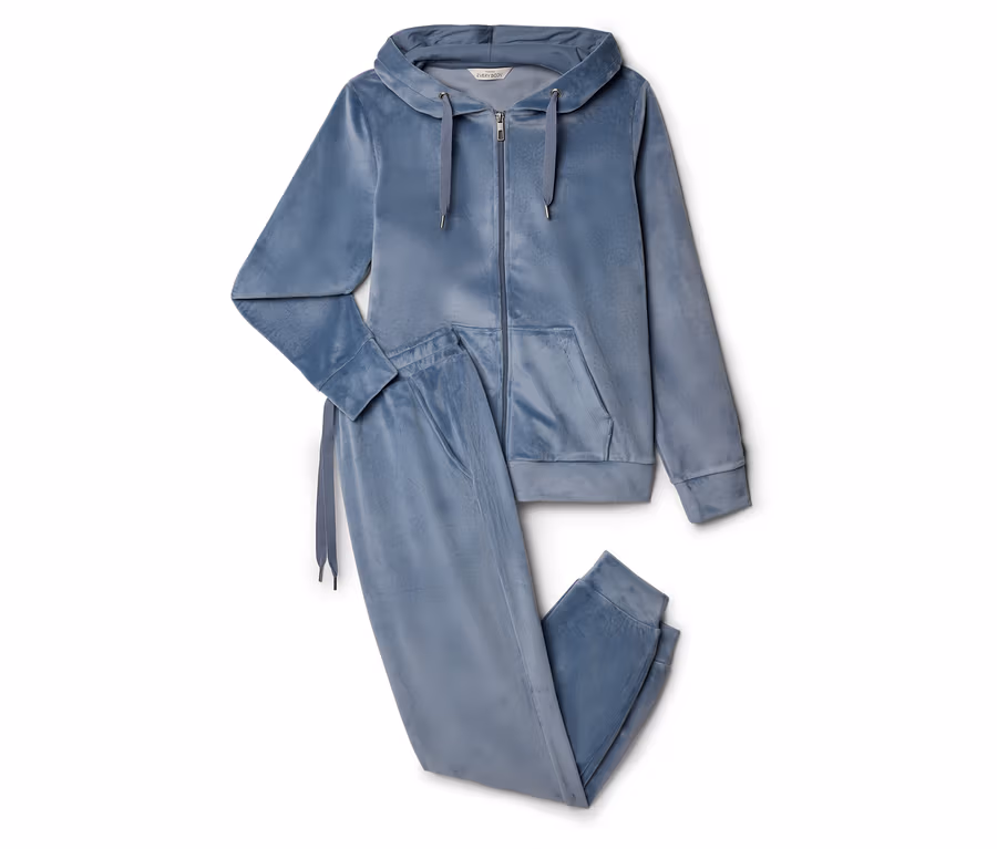 Ein blaues Samt-Trainingsanzug-Set mit Kapuzenjacke mit Reißverschluss und Kordelzug sowie Jogginghose liegt auf einem weißen Hintergrund.