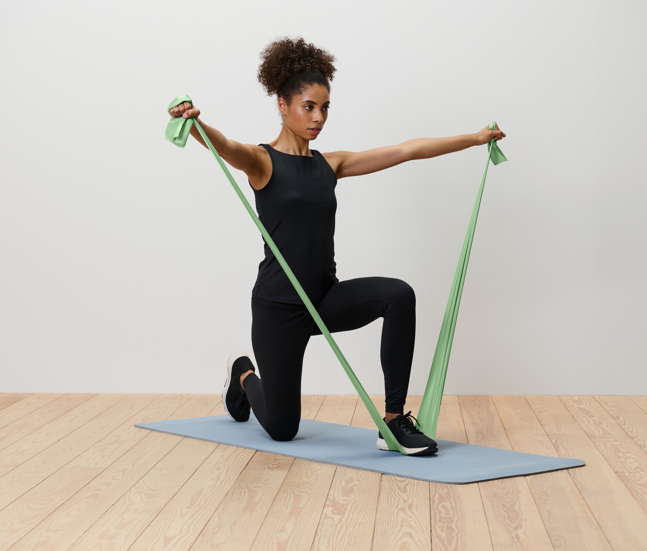 Eine Frau kniet auf einer blauen Yogamatte und dehnt ein grünes Widerstandsband.