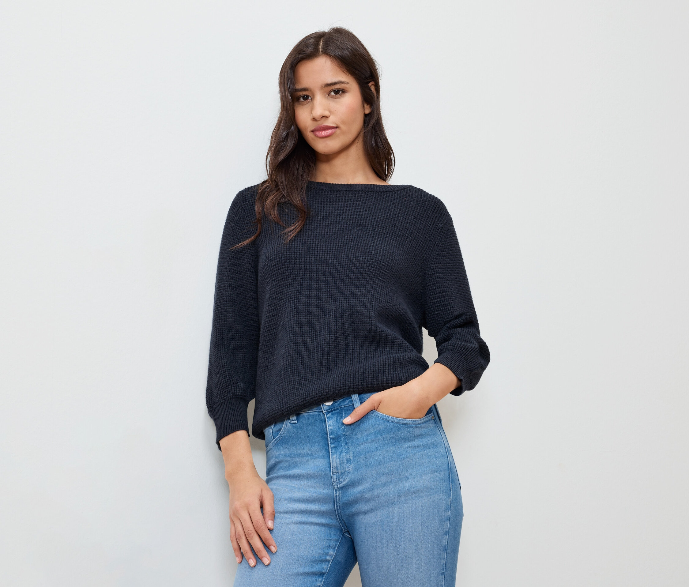 Frau mit einer Hand in der Hosentasche, trägt einen dunkelblauen Feinstrickpullover.