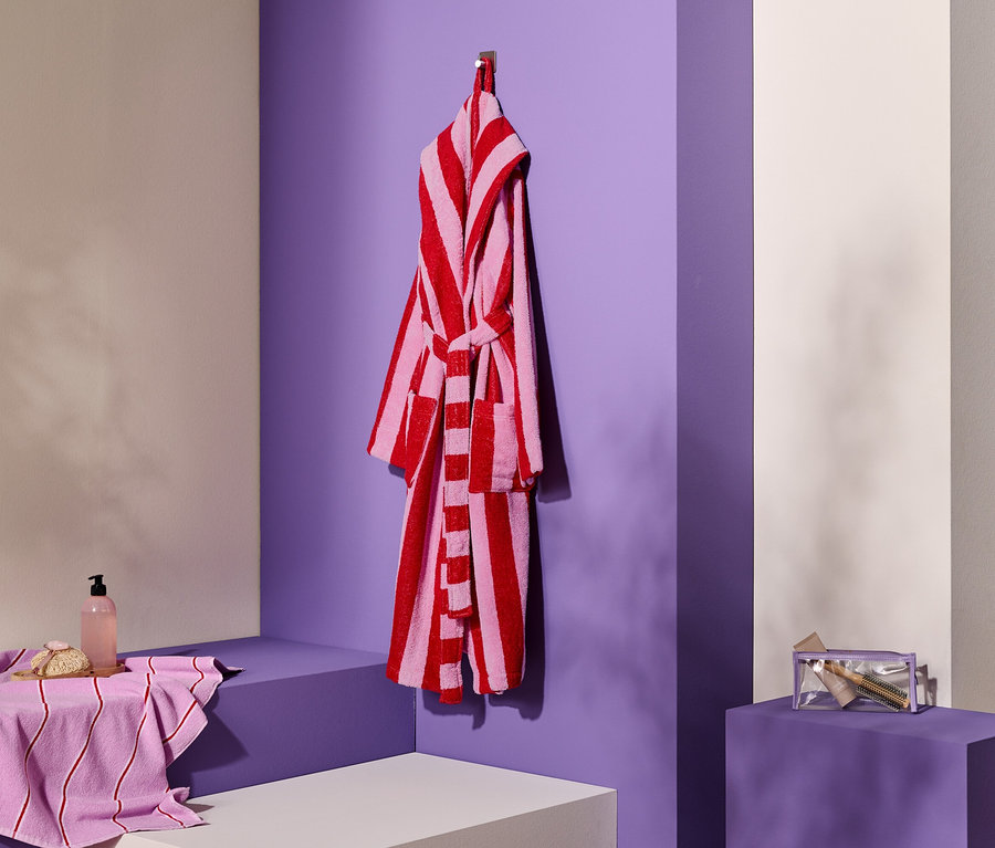 Gestreifter Bademantel hängt an Haken neben Handtuch, Seife und Kosmetiktasche.